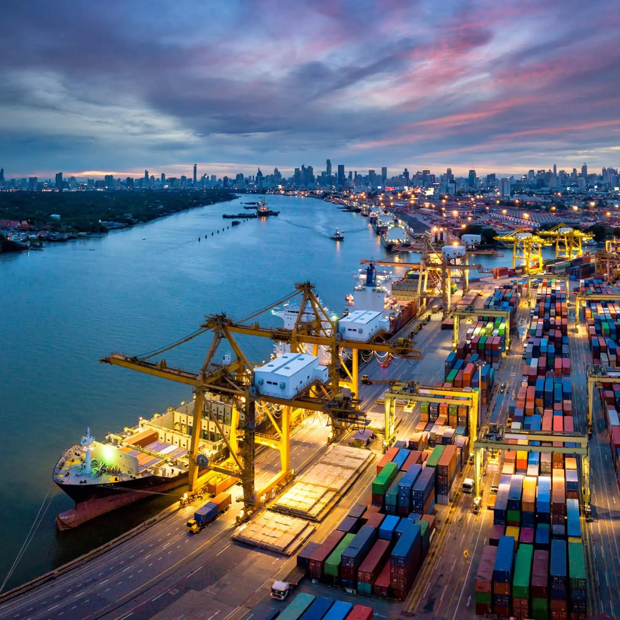 Aerial view of a container port at dusk, with gantry cranes and a docked container ship.